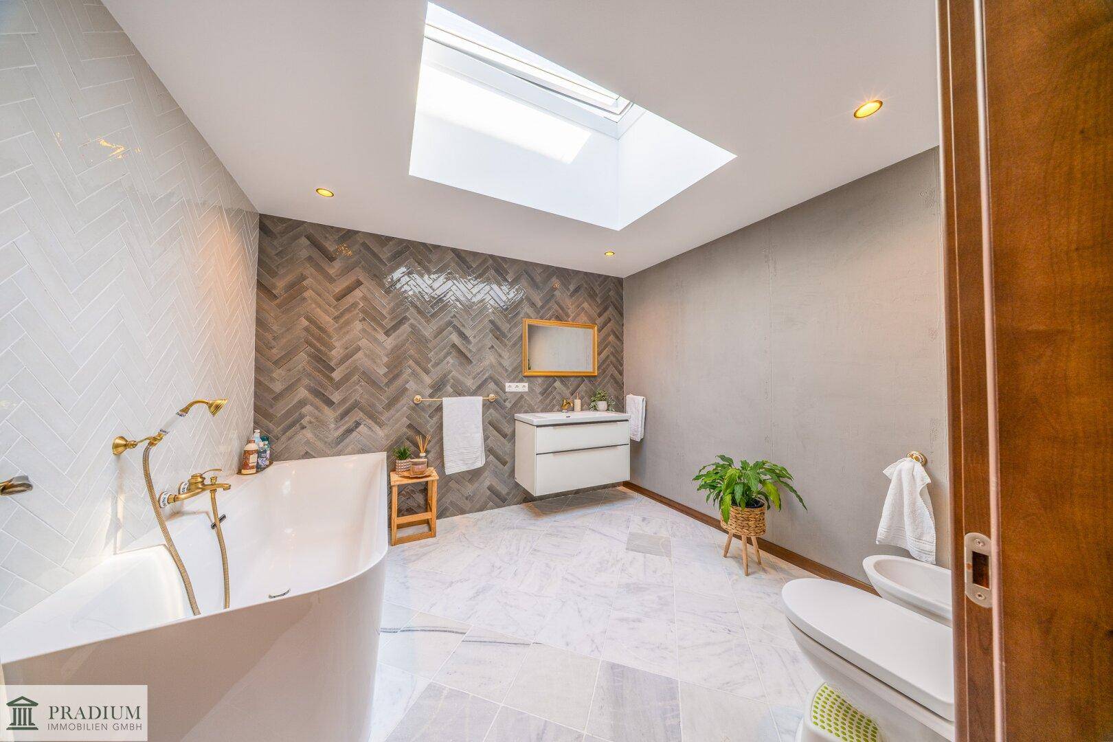 Modernes Badezimmer mit freistehender Badewanne, Dachfenster und stilvollen Fliesen in Marmoroptik.