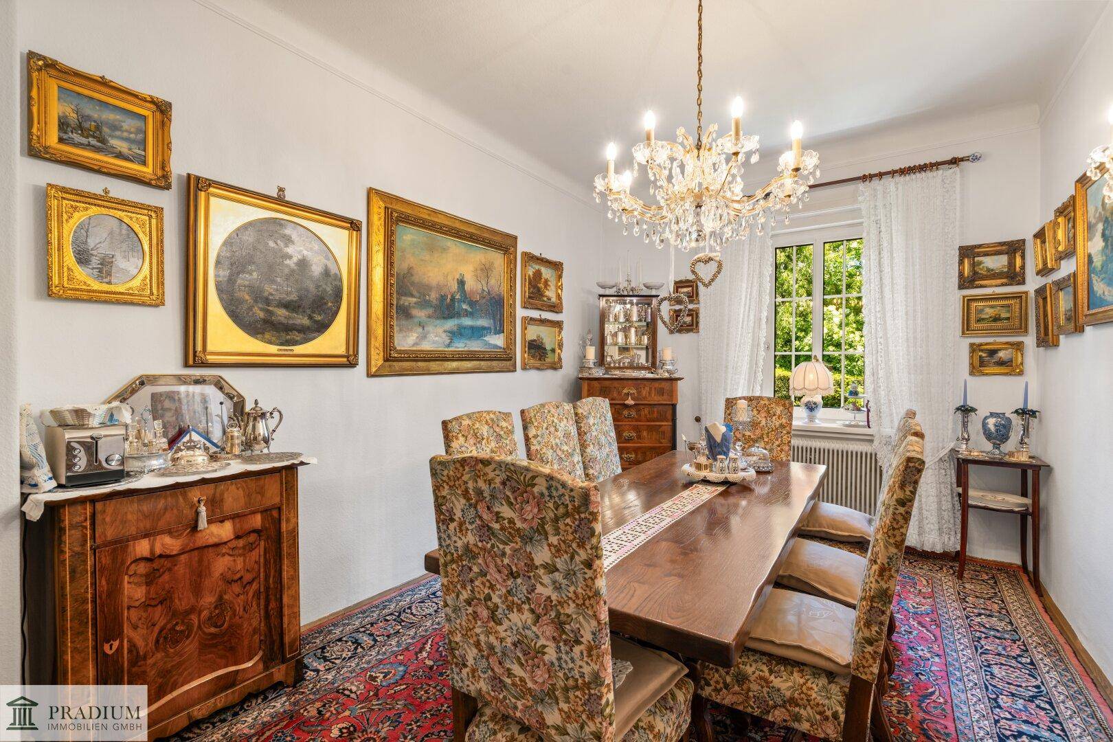 Klassisches Esszimmer mit großem Holztisch, floral gemusterten Stühlen und vielen gerahmten Bildern.