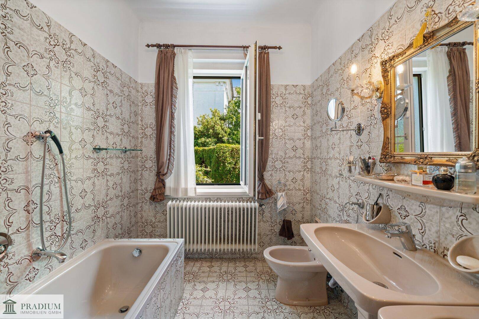 Klassisches Badezimmer mit gemusterten Fliesen, Badewanne, Bidet und Fenster mit Gartenblick.