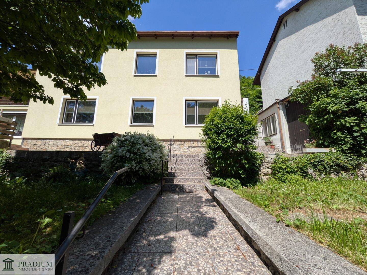 Vorderansicht des Hauses mit Treppenzugang und gepflegter Grünfläche.