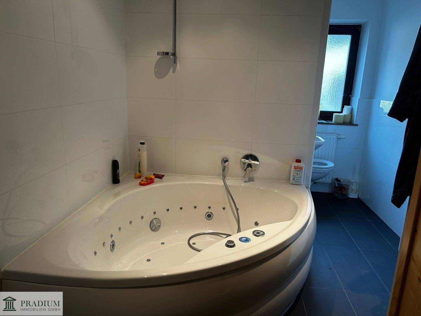 Badezimmer mit Eck-Whirlpool-Badewanne, dunklen Fliesen und einem Fenster für Tageslicht.