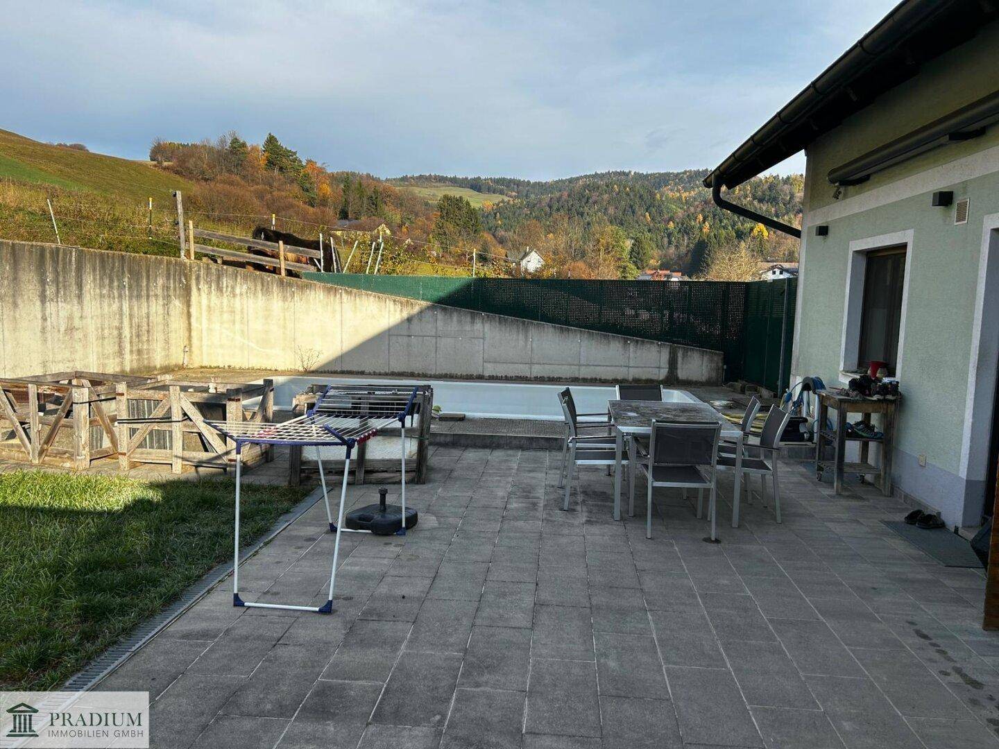 Gepflasterte Terrasse mit Esstisch, Stühlen und kleinem Pool, umgeben von grünen Hügeln.
