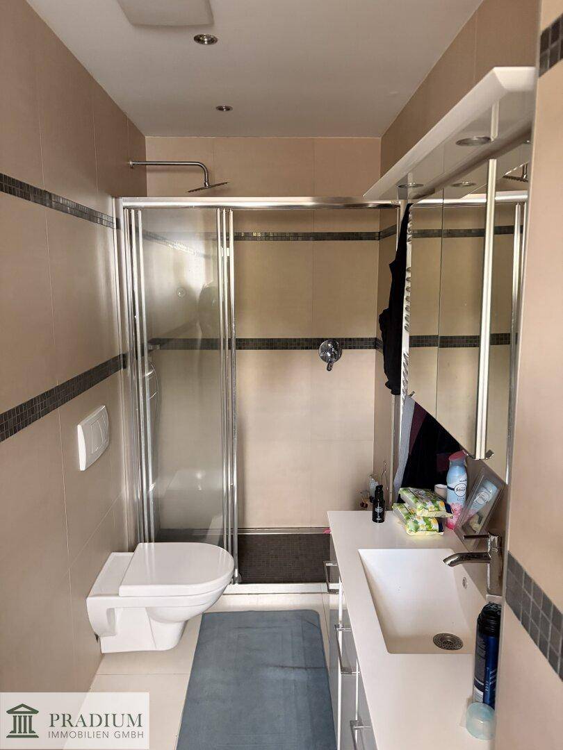 Modernes Badezimmer mit Duschkabine, WC, Einzelwaschbecken und beigefarbenen Fliesen.