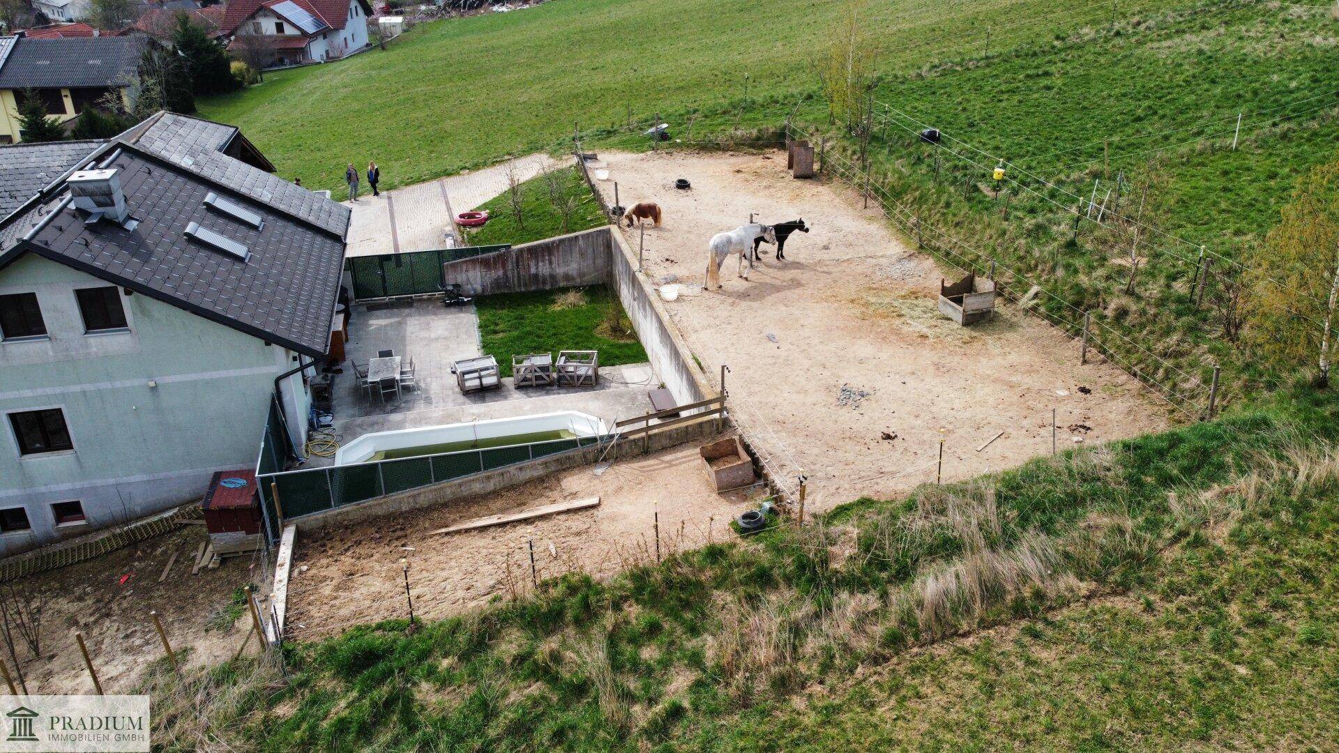 Luftaufnahme eines Anwesens mit Haus, kleinem Pool, Terrasse und weitläufigem Pferdebereich.