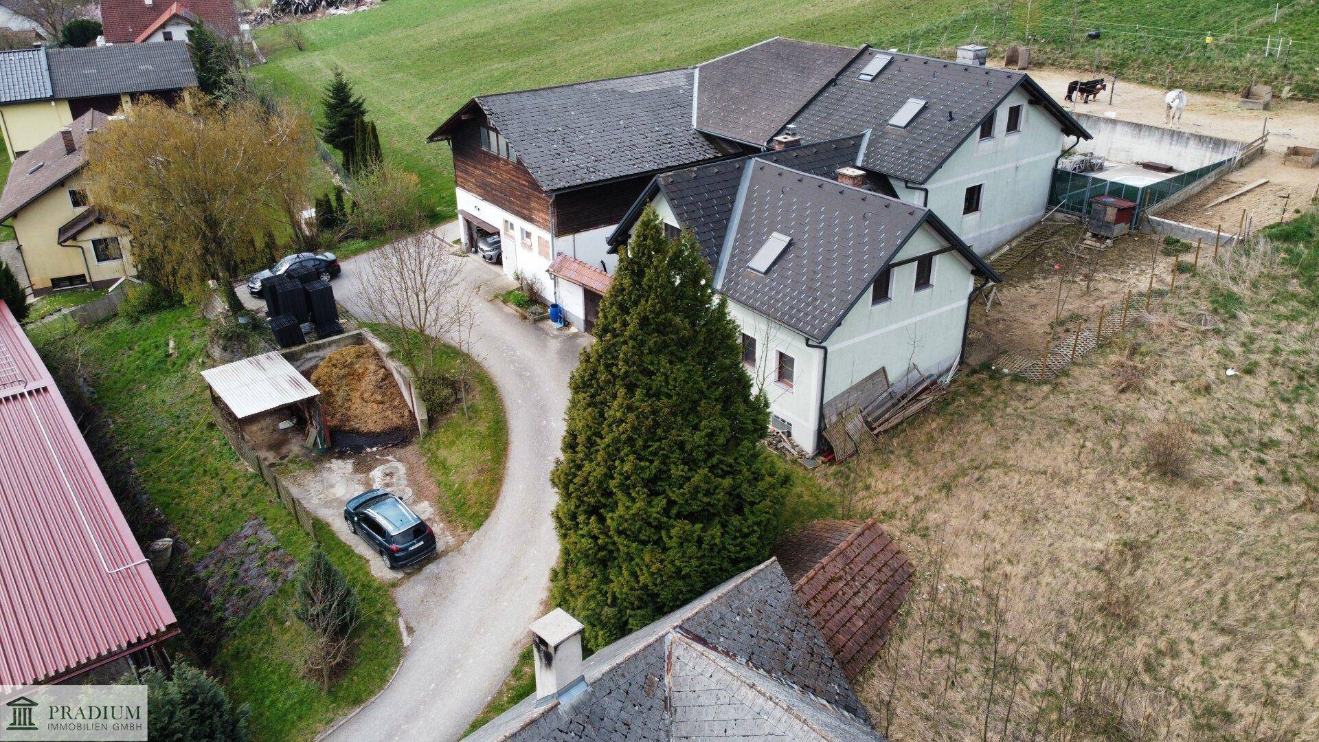Weitläufige Luftaufnahme des Anwesens mit mehreren Gebäuden, Zufahrt und grüner Umgebung.