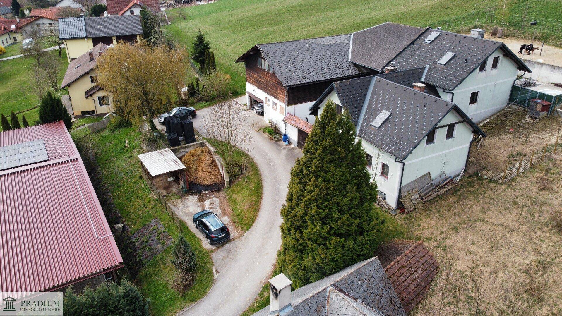 Weitläufige Luftaufnahme des Anwesens mit mehreren Gebäuden, Zufahrt und grüner Umgebung.