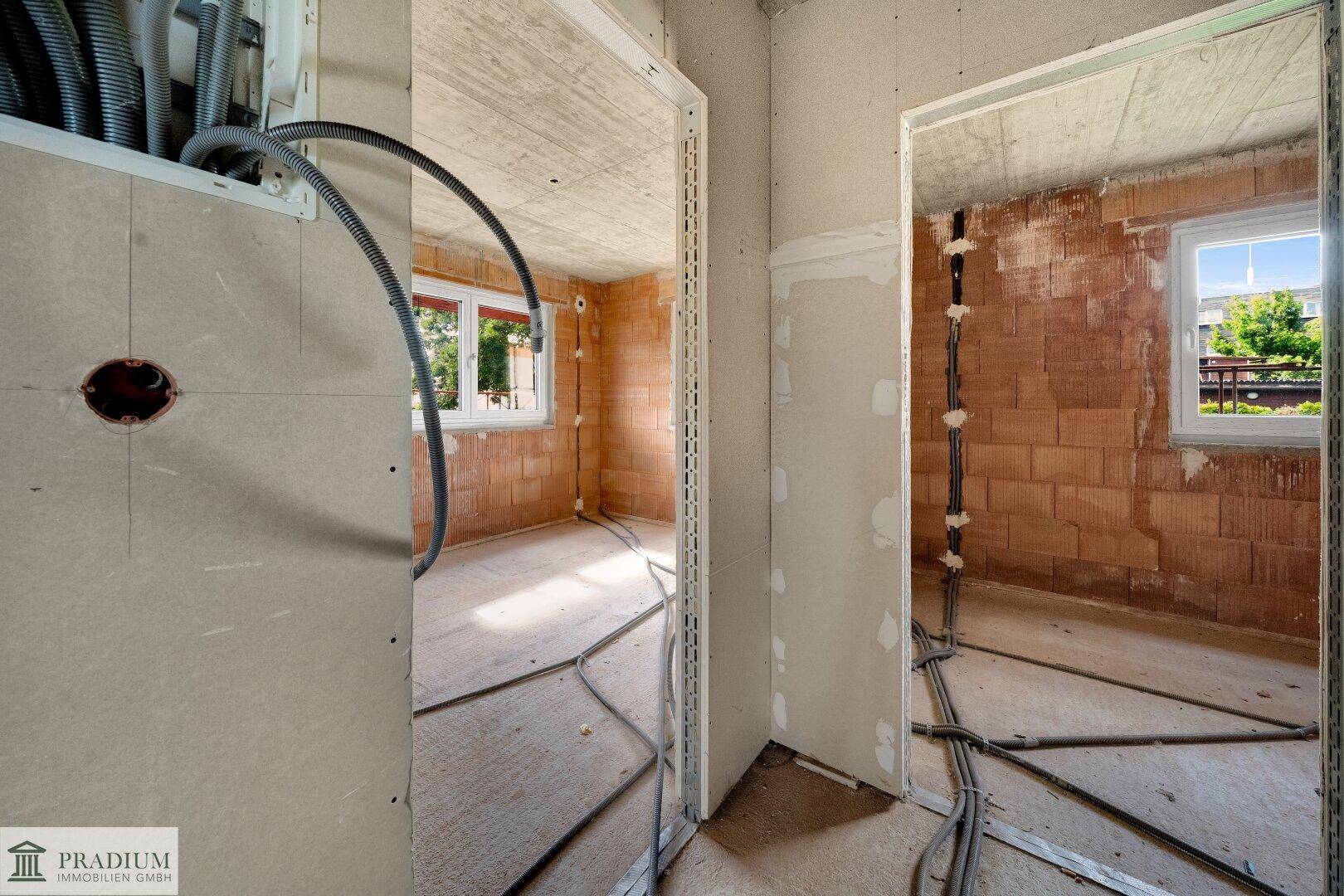 Innenräume im Rohbau mit Türöffnungen, unverputzten Wänden und sichtbaren Kabeln.