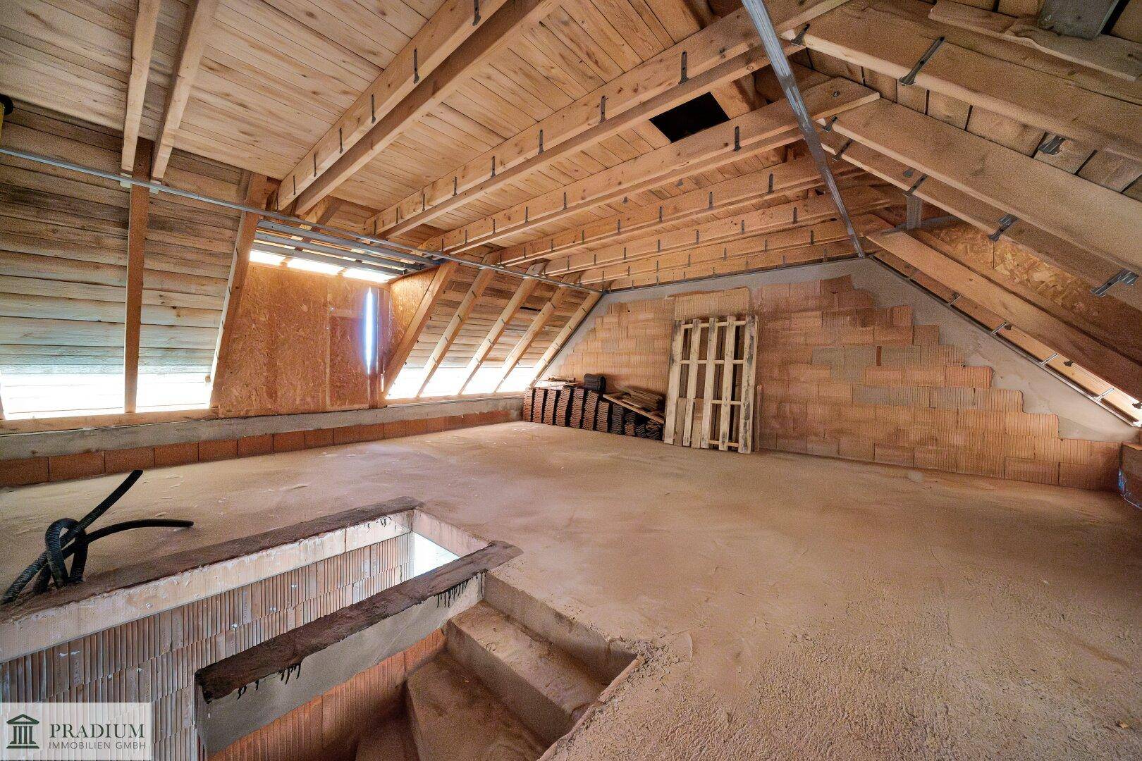 Dachboden im Rohbau mit sichtbarer Holzkonstruktion, Dachschrägen und Betonboden.