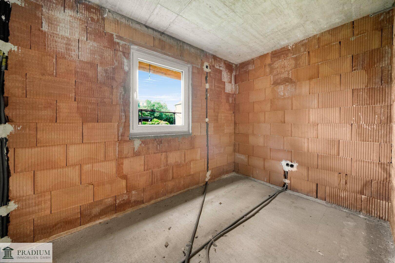 Kleiner Rohbau-Raum mit einem Fenster, unverputzten Ziegelwänden und sichtbaren Kabeln.