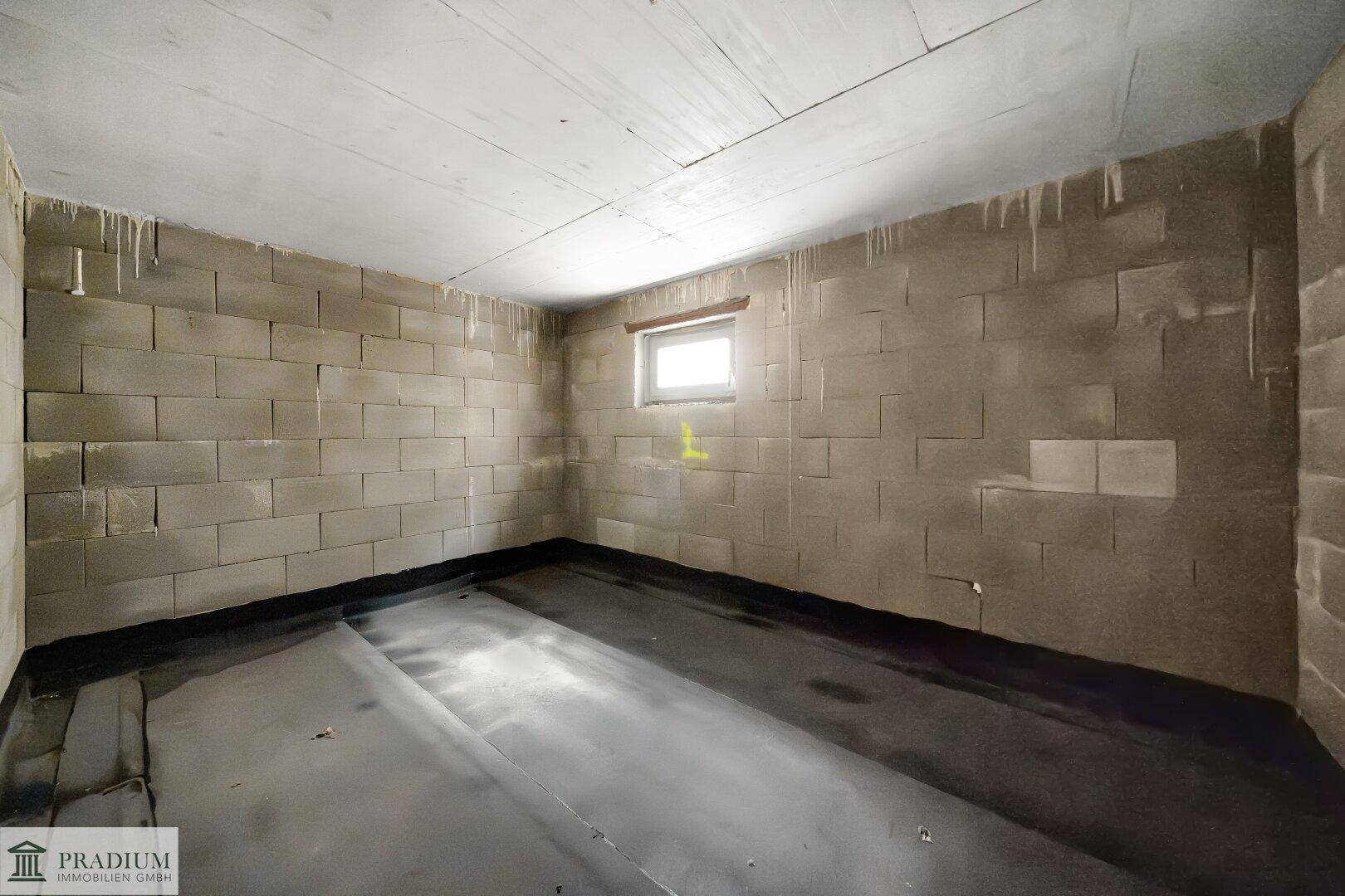 Kellerraum im Rohbau mit kleinen Fenstern, Betonwänden und dunklem Bodenbelag.