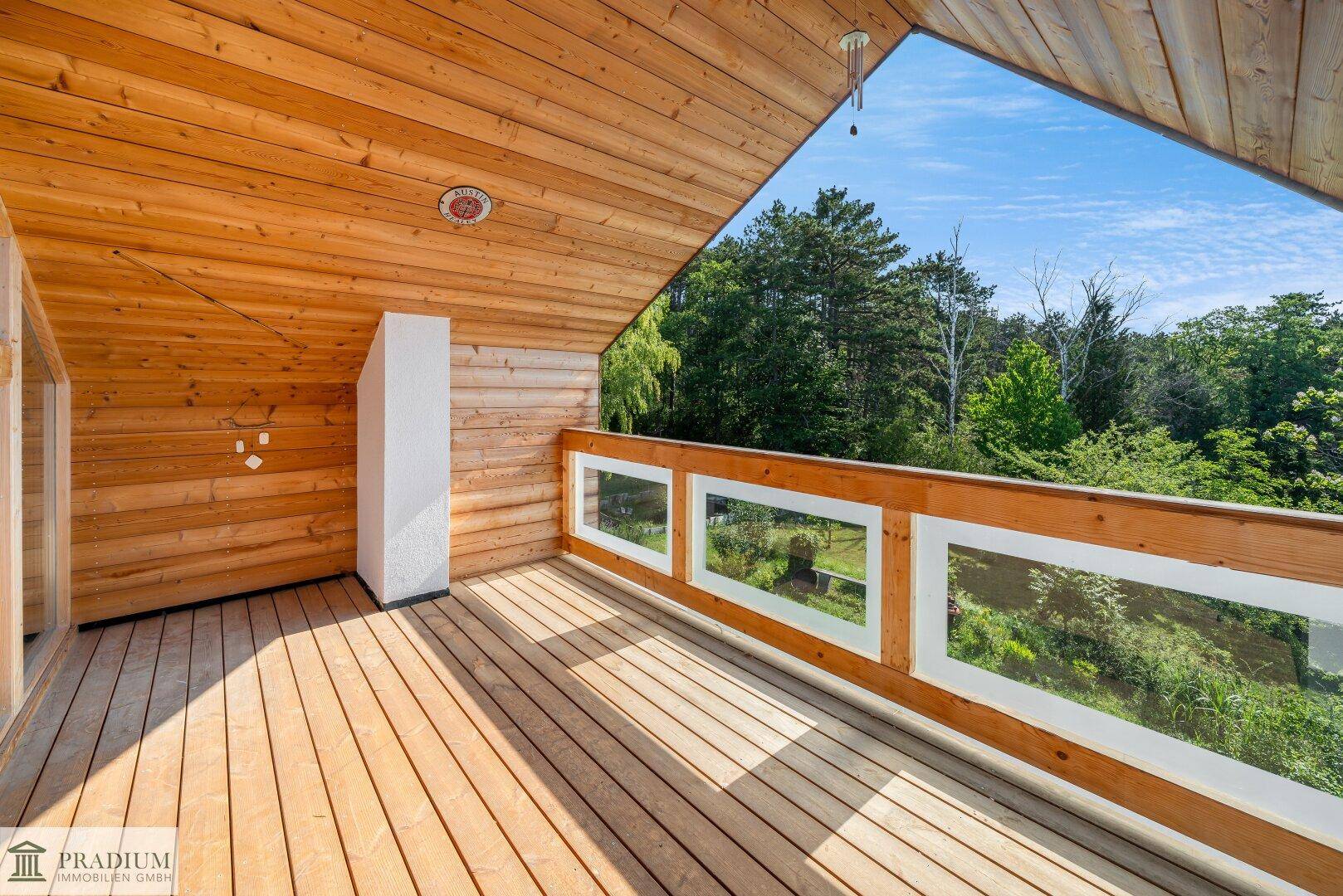 Holzverkleideter Balkon mit Glasgeländer und weitem Blick in die grüne Natur.
