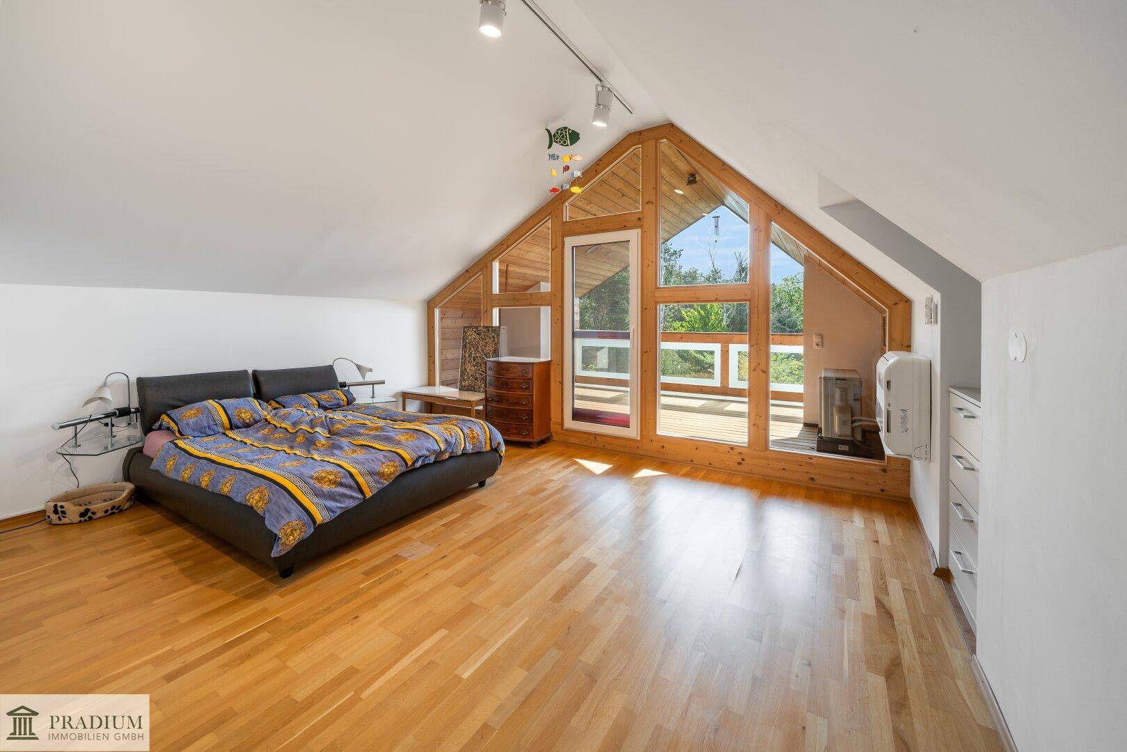 Helles Schlafzimmer im Dachgeschoss mit Holzboden, großen Fenstern und Balkonzugang.