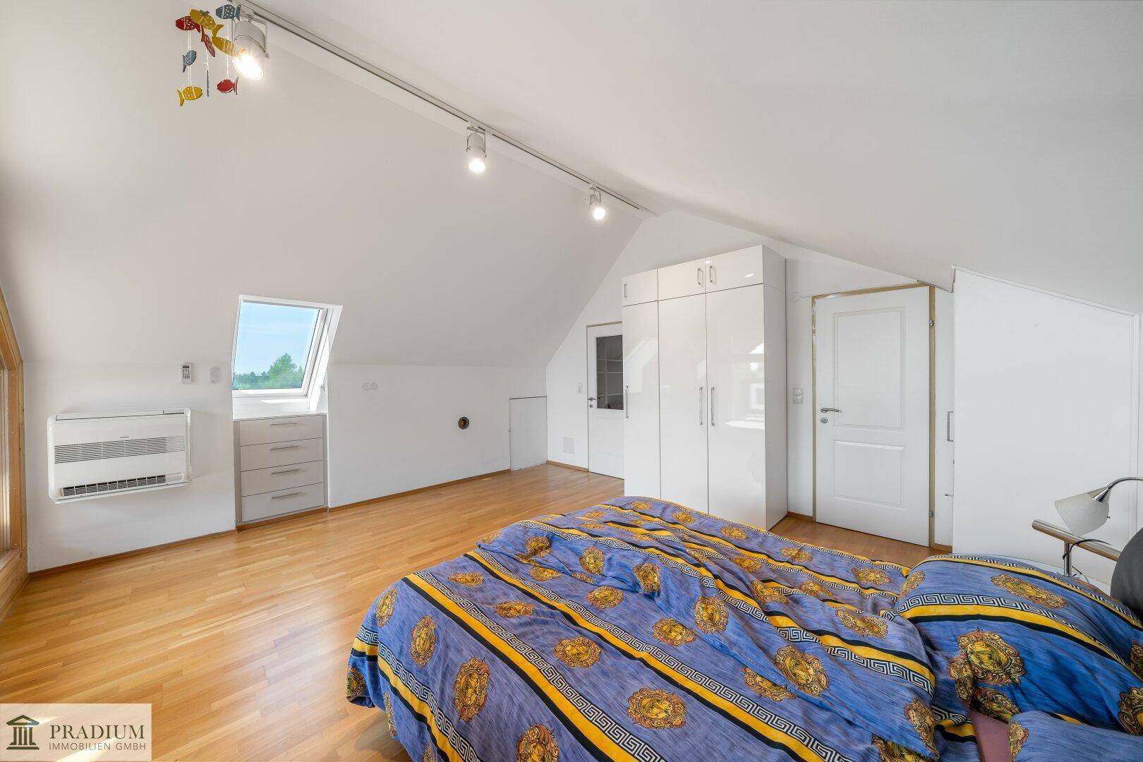 Geräumiges Schlafzimmer im Dachgeschoss mit Holzboden, Dachfenster und weißem Kleiderschrank.