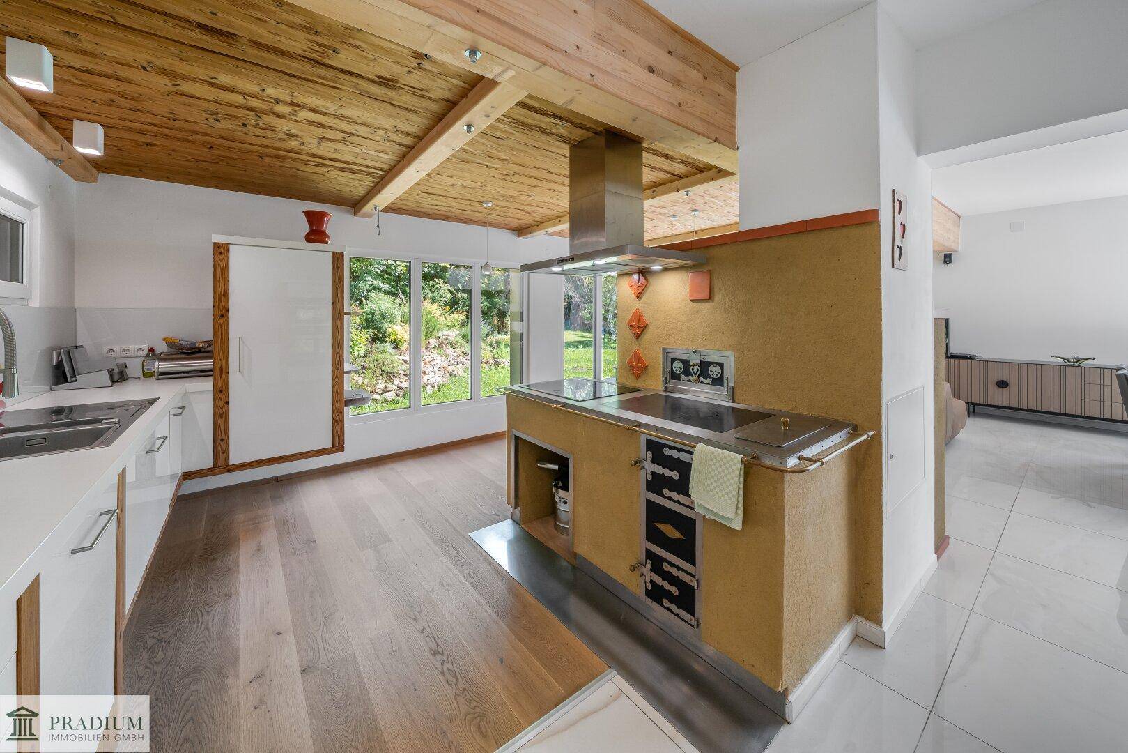 Moderne Küche mit Holzbalkendecke, integriertem Herd und Blick ins Grüne.