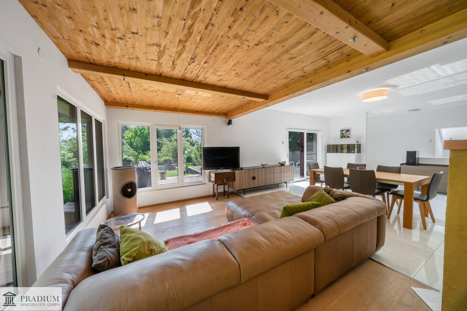 Gemütlicher Wohnbereich mit Ledersofa, Holzbalkendecke und großen Fenstern zum Garten.