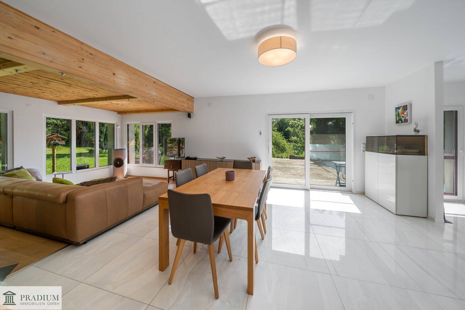 Heller Wohn- und Essbereich mit Holzbalkendecke, großen Fenstern und Zugang zur Terrasse.