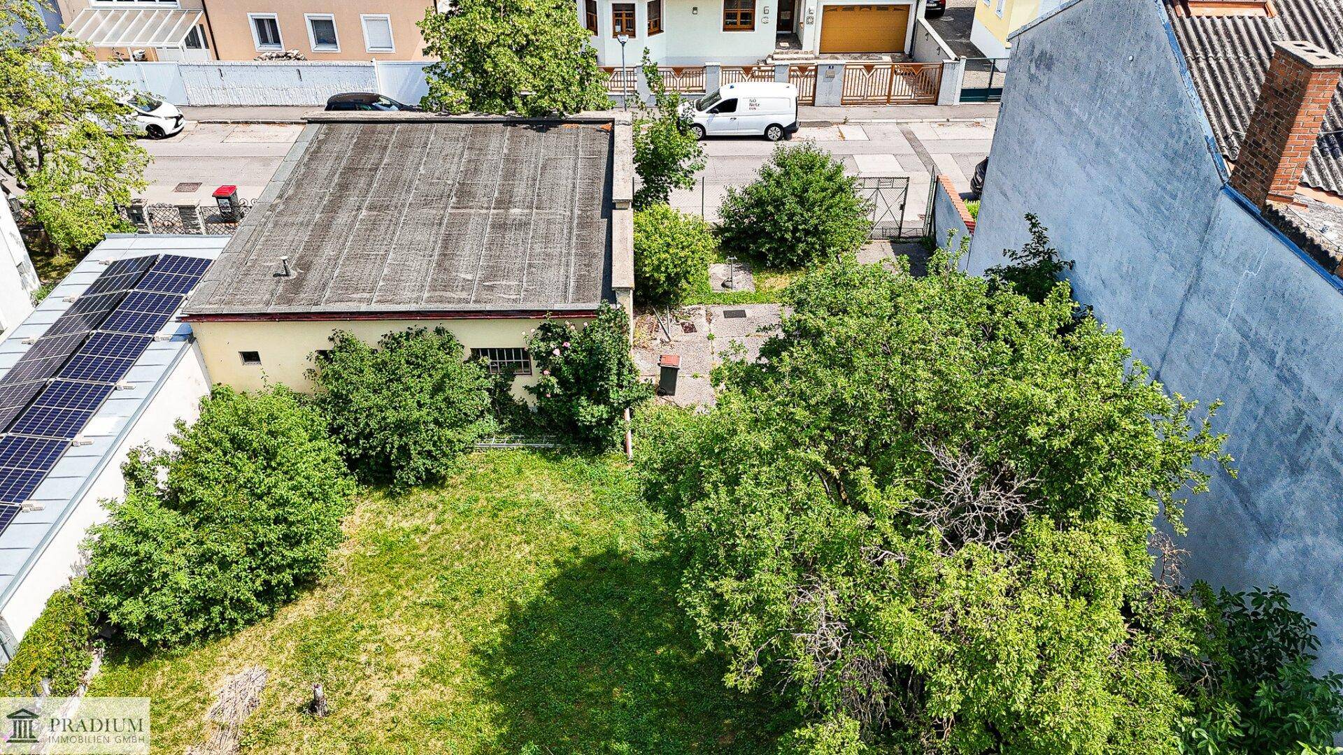 Übersicht des Gartengrundstücks von oben, mit viel Grün, Bäumen und einem Gebäude mit Solarmodulen im Vordergrund.