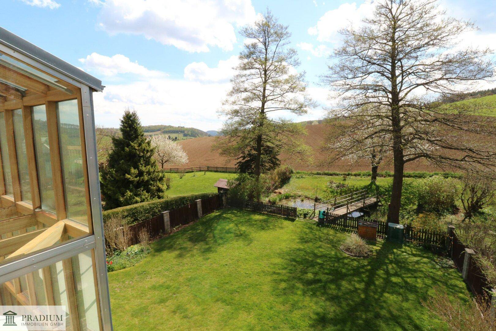 Weitläufiger Blick vom Haus auf den Garten, Teich und die umliegende grüne Landschaft.