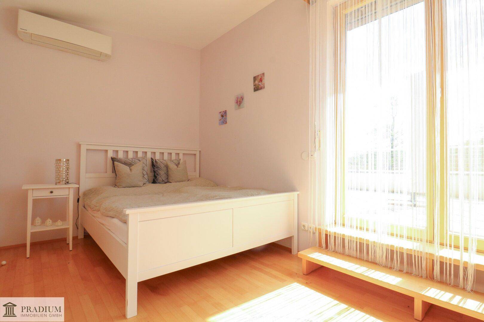 Helles Schlafzimmer mit weißem Bett, Holzfußboden und großem Fenster für viel Tageslicht.