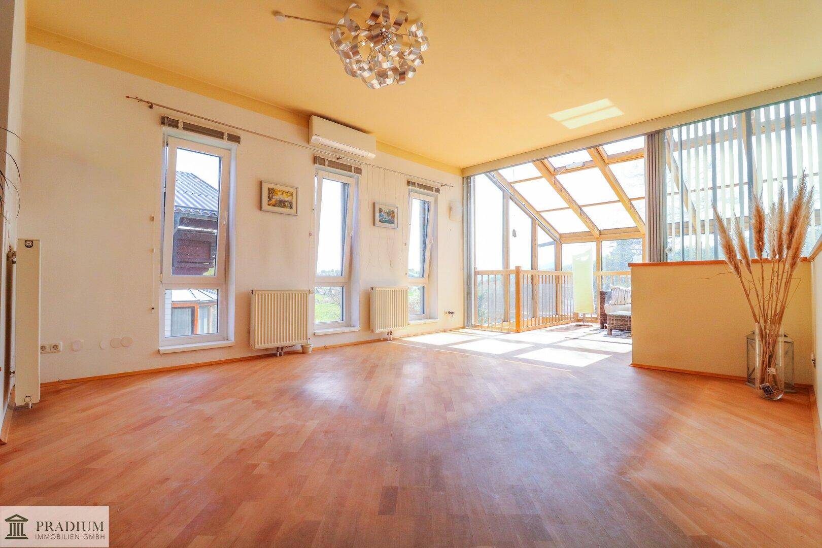 Geräumiges Wohnzimmer mit hellem Parkettboden, Klimaanlage und Zugang zum Wintergarten.