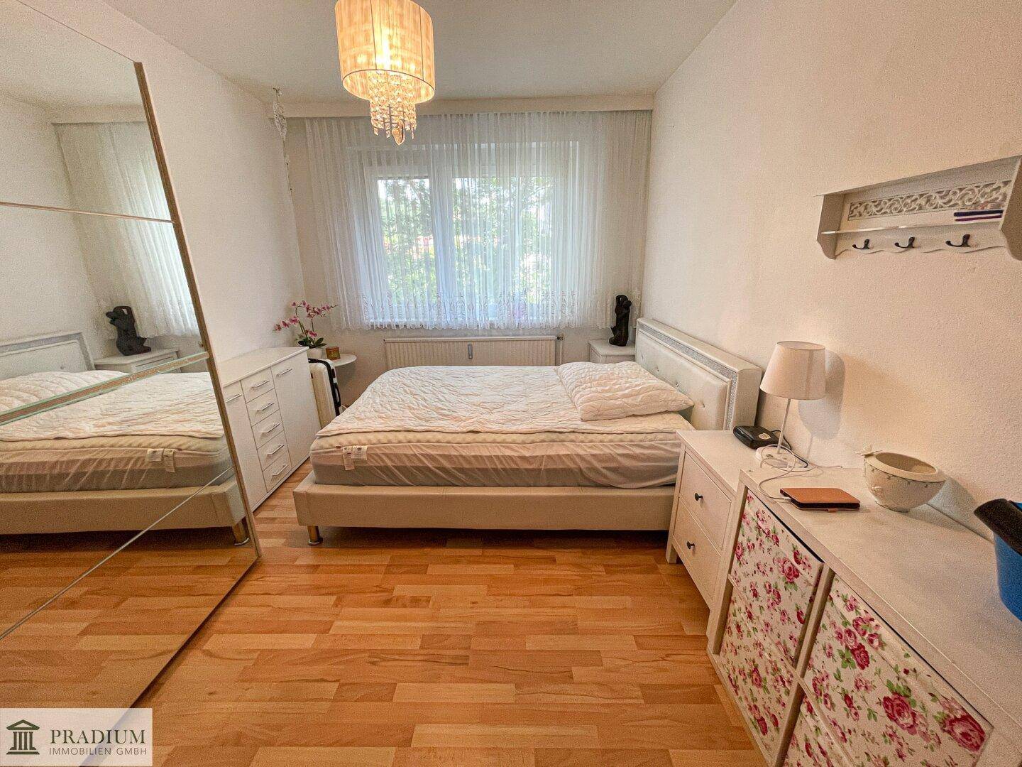 Helles Schlafzimmer mit Doppelbett, weißen Möbeln und großem Spiegelschrank, Holzboden.
