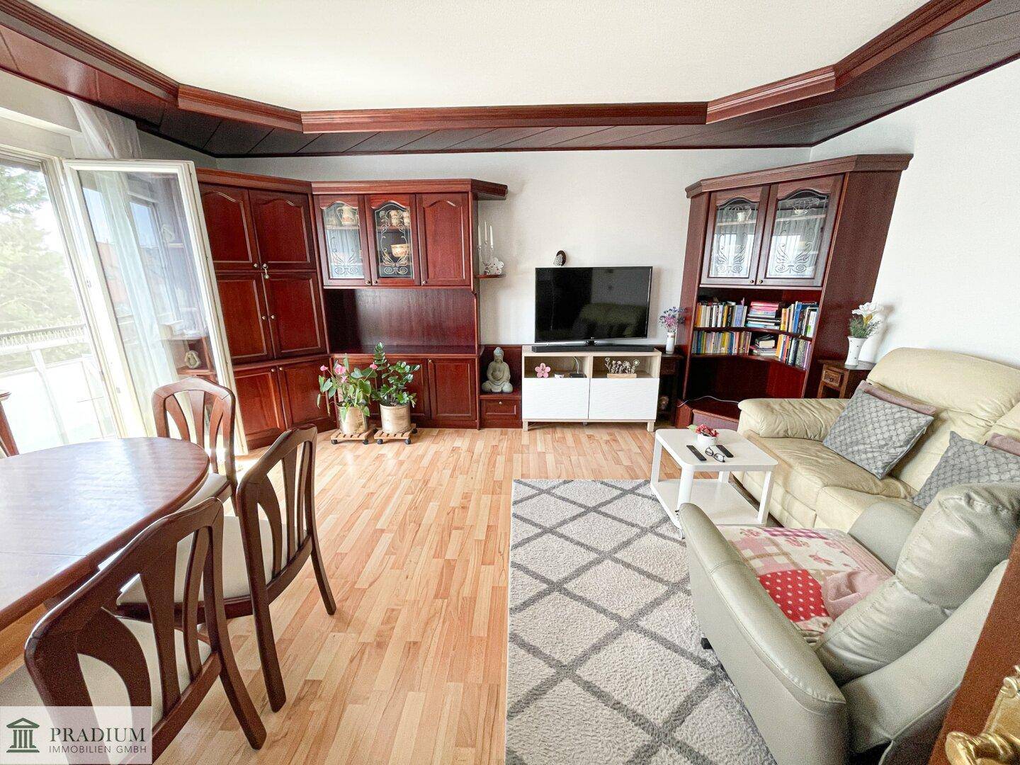 Gemütlicher Wohnbereich mit Sofa, Fernseher und dunklen Holzmöbeln, angrenzend an den Essbereich.
