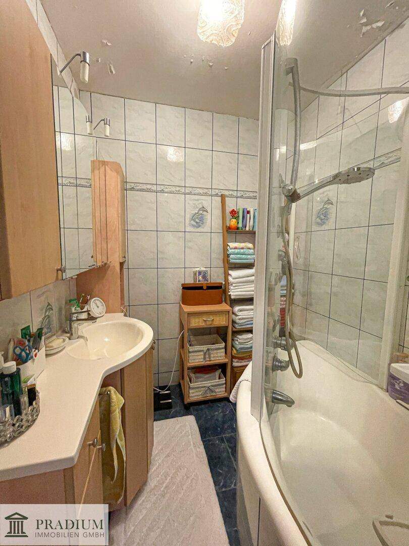 Badezimmer mit Badewanne, Duschabtrennung, Waschbecken und hellen Wandfliesen.