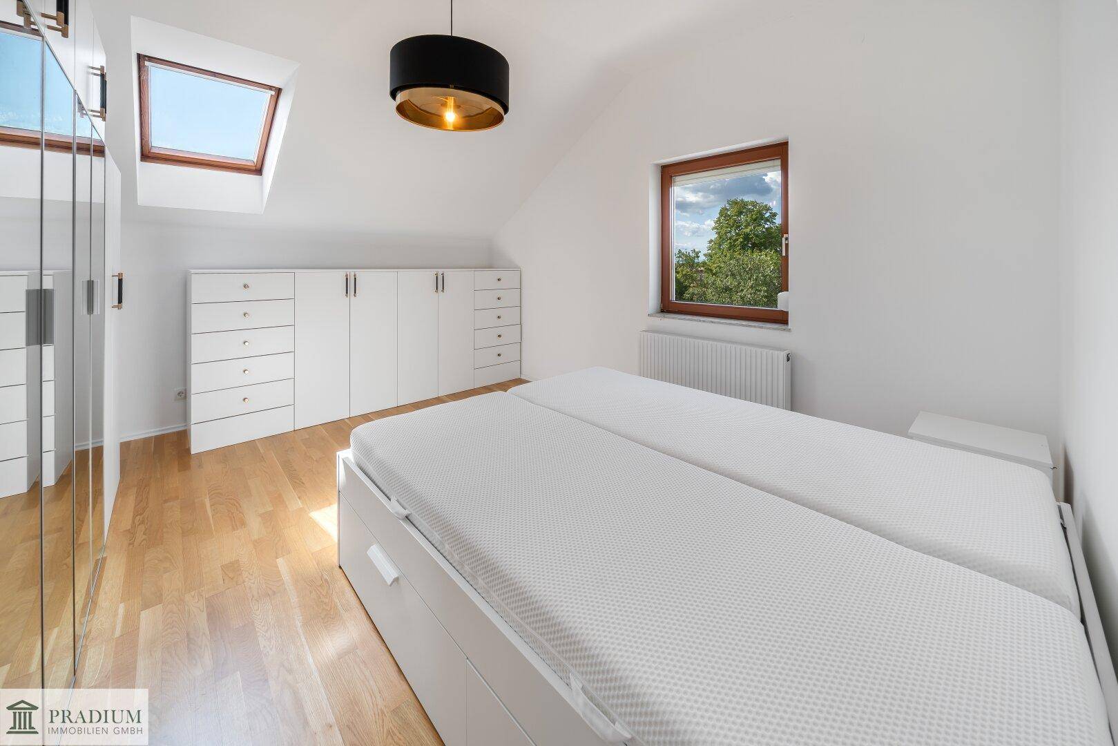 Helles Schlafzimmer im Dachgeschoss mit Holzboden, Dachfenster und weißen Einbauschränken.