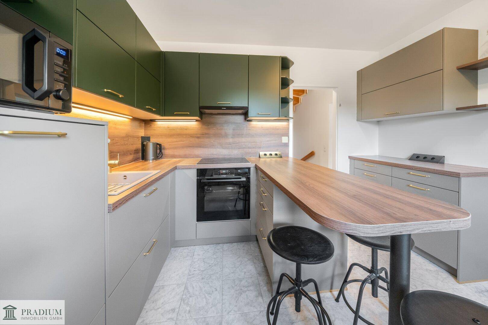Moderne Küche mit dunkelgrünen und grauen Schränken, Holzarbeitsplatte und Frühstücksbar.