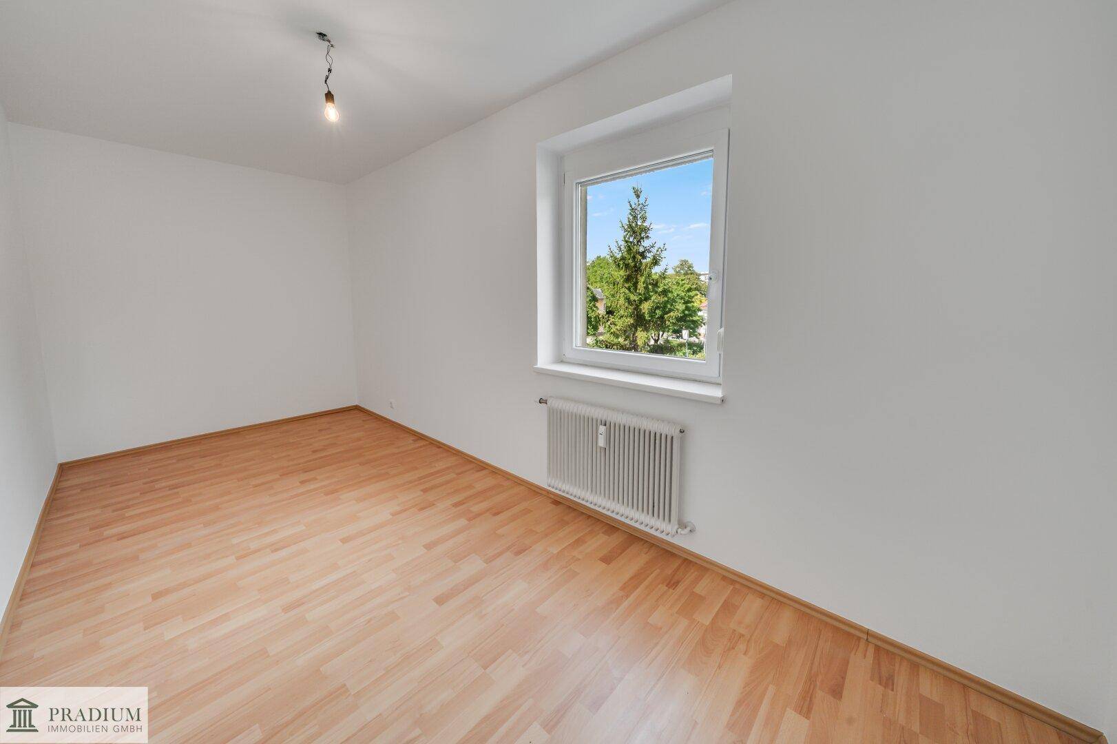 Gemütliches Zimmer mit Laminatboden und großem Fenster, bietet eine ruhige Atmosphäre.