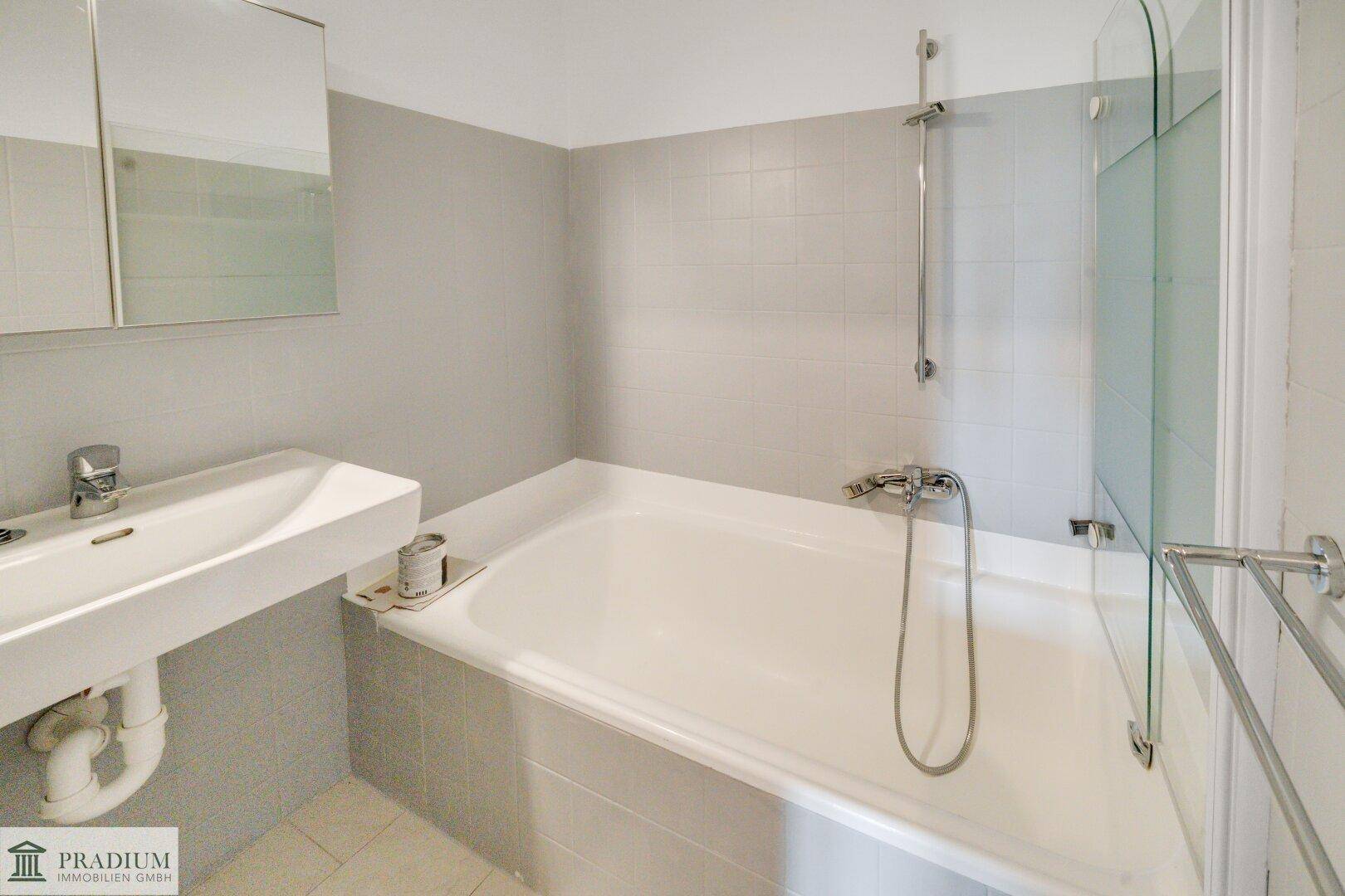Modernes Badezimmer mit Badewanne, Waschbecken und Spiegelschrank, in hellen Grautönen gehalten.