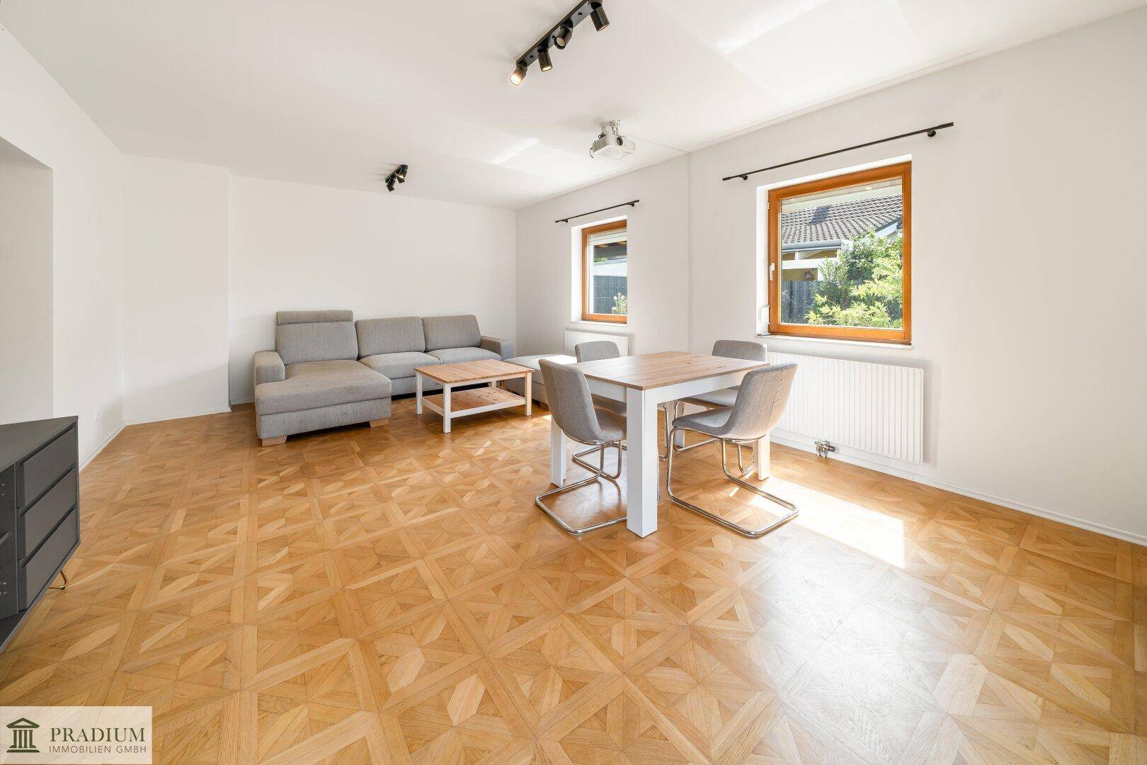 Geräumiger Wohnbereich mit Esstisch, Sofa und Blick ins Grüne durch die Fenster.