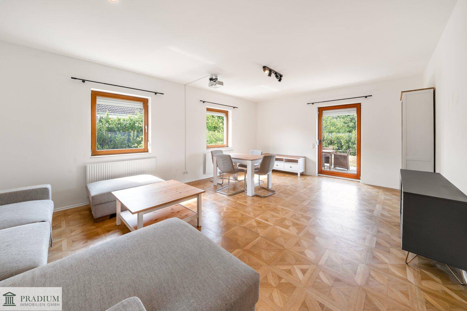 Heller Wohn- und Essbereich mit Parkettboden, großen Fenstern und Zugang zur Terrasse.