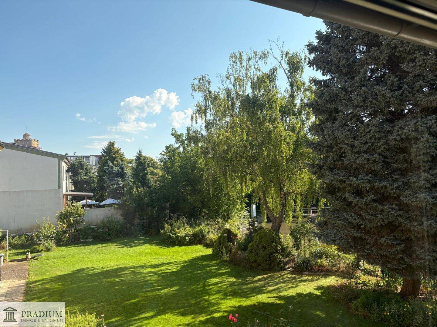 Großer, gepflegter Garten mit Rasenfläche und altem Baumbestand unter blauem Himmel.