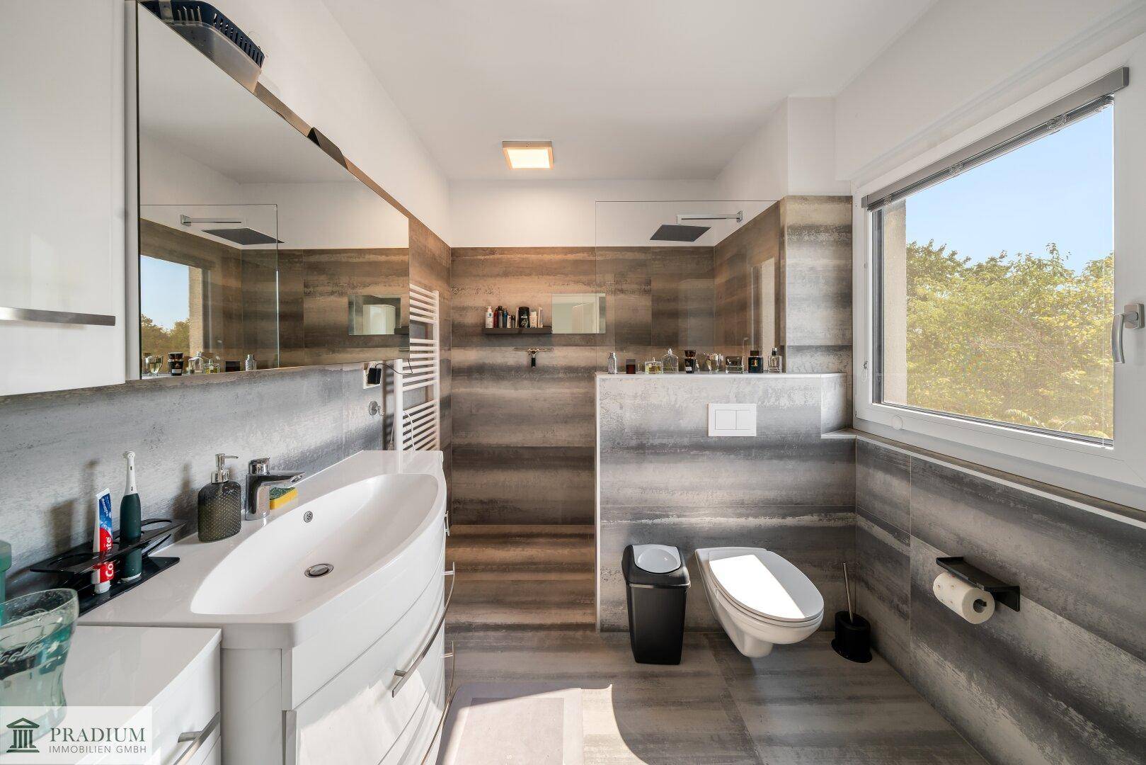 Modernes Badezimmer mit grauen Fliesen, Einzelwaschbecken, wandhängendem WC und Fenster.