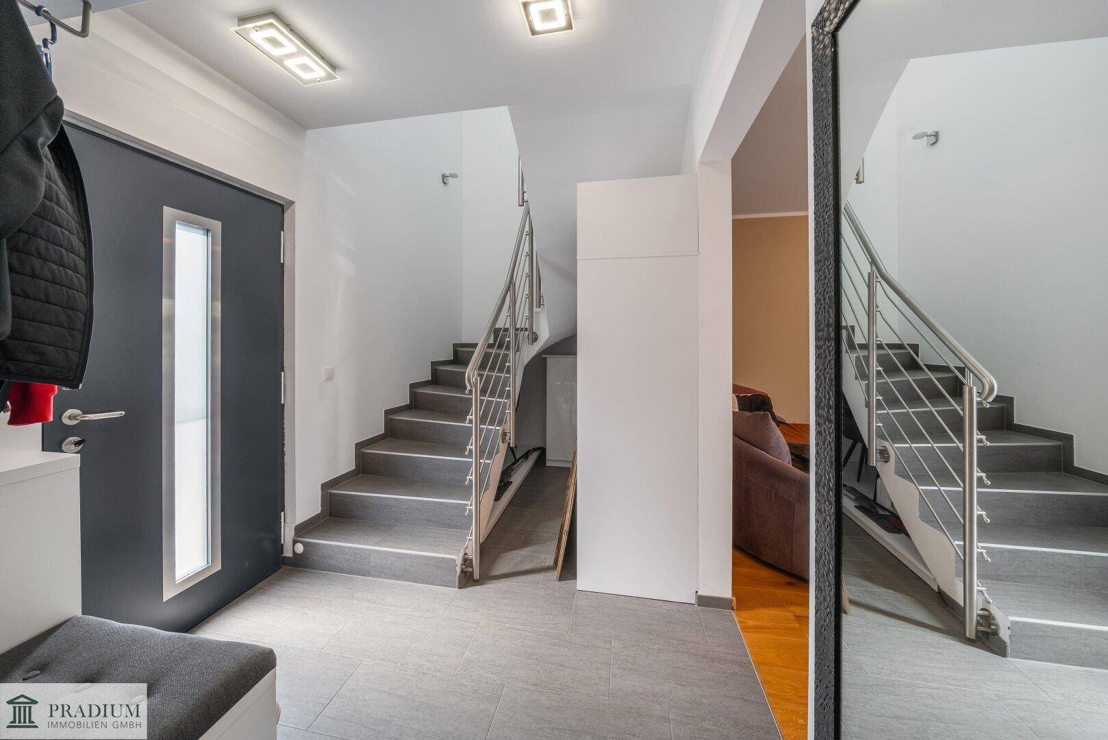 Heller Eingangsbereich mit moderner Treppe, dunkler Haustür und barrierefreier Rampe.