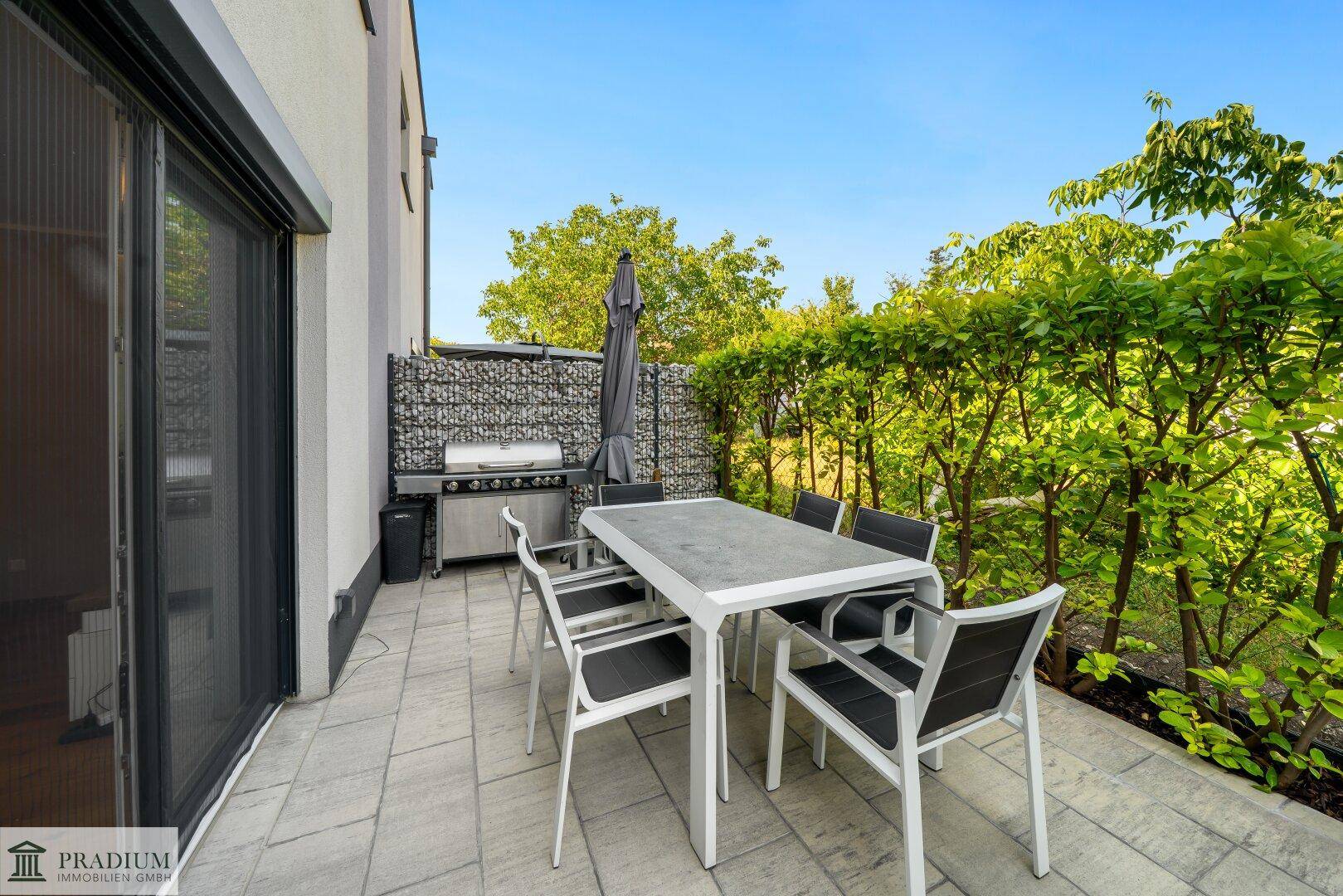 Sonnenterrasse mit Esstisch, Grillbereich und grüner Hecke für Privatsphäre im Freien.