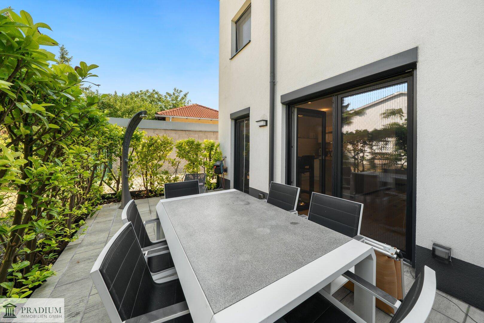 Geräumige Terrasse mit Gartenmöbeln und Blick auf die moderne Hausfassade und den Garten.