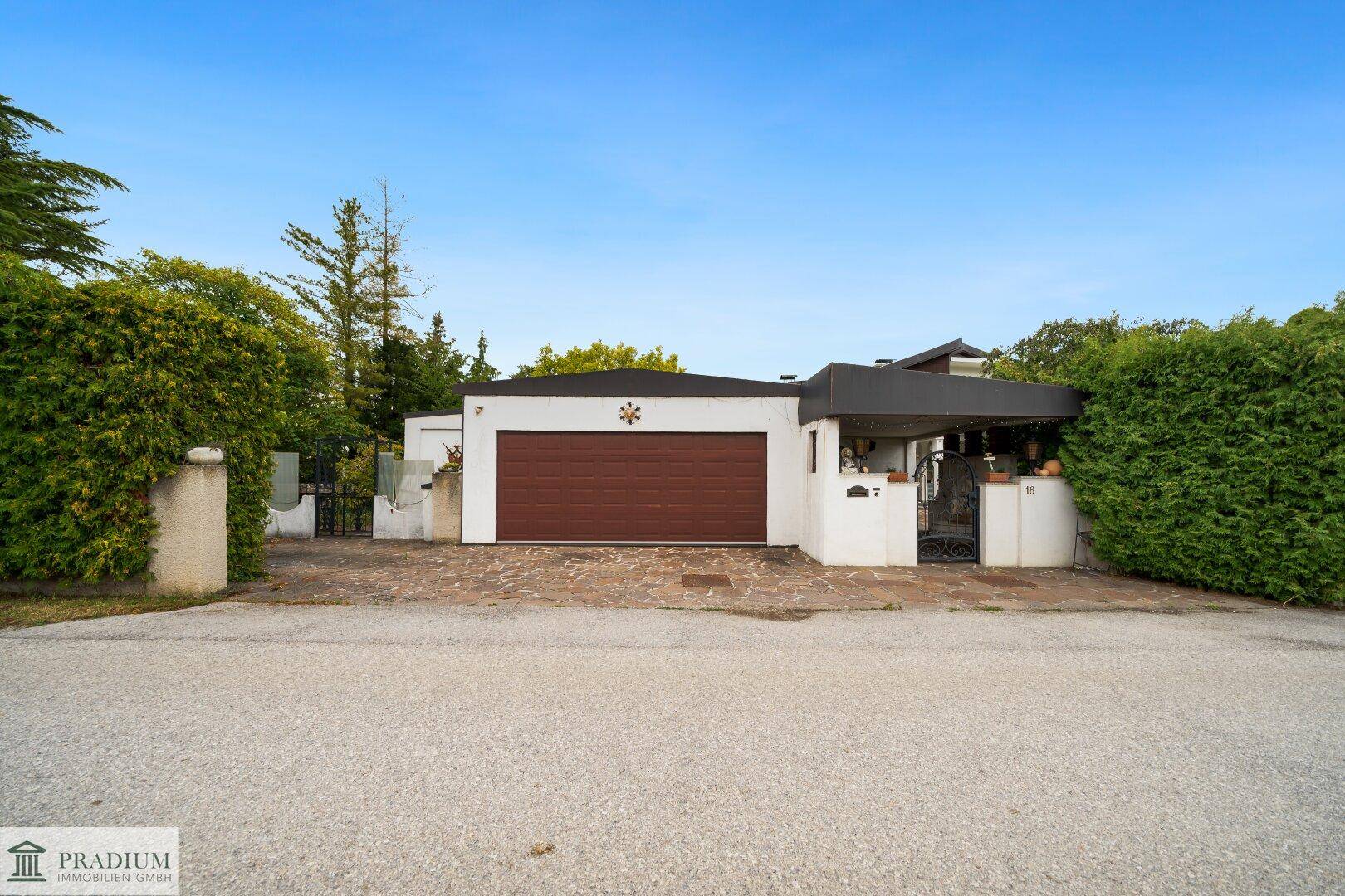 Vorderansicht des Hauses mit Garage, Carport und gepflegter Hecke entlang der Einfahrt.