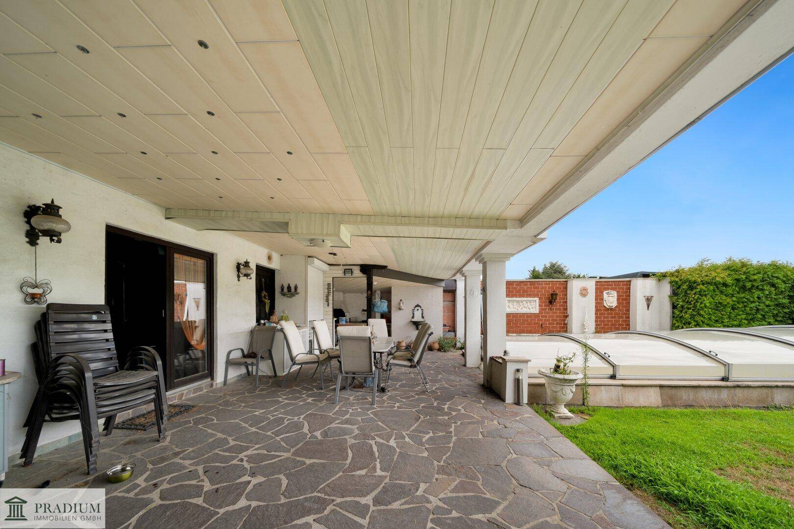 Überdachte Terrasse mit Steinfliesenboden und Gartenmöbeln, ideal für entspannte Stunden im Freien.