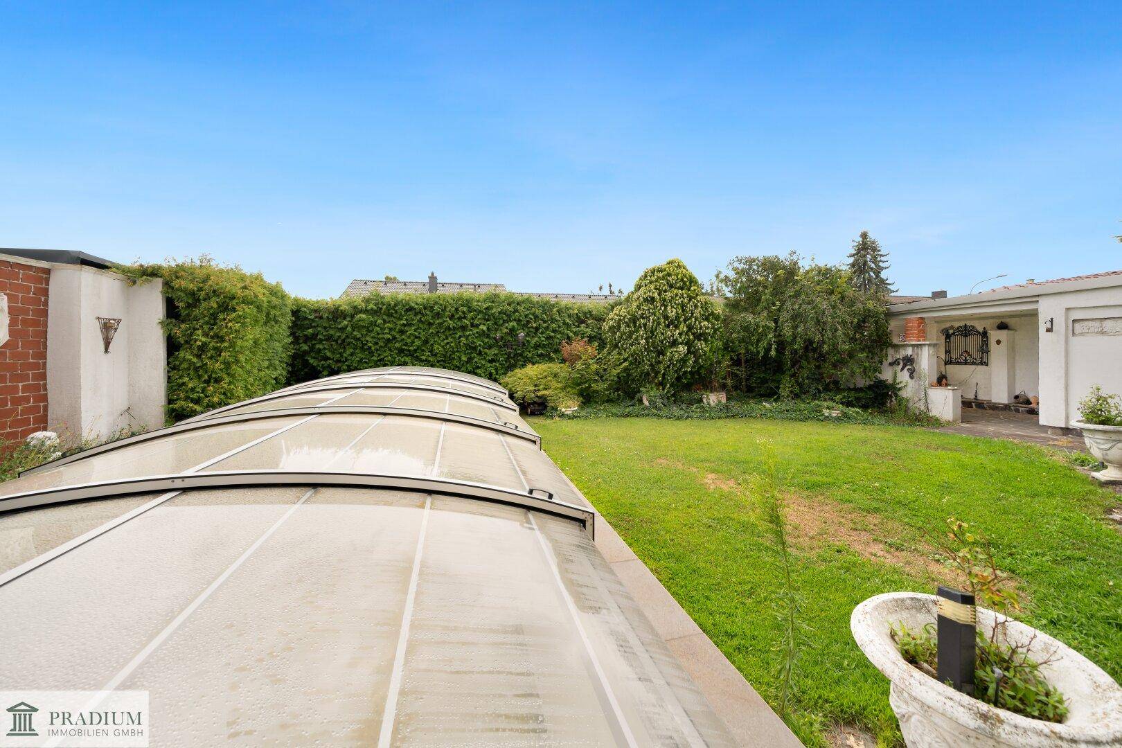 Blick über den Rasen und die Abdeckung des Pools im Garten, umgeben von hohen Hecken.