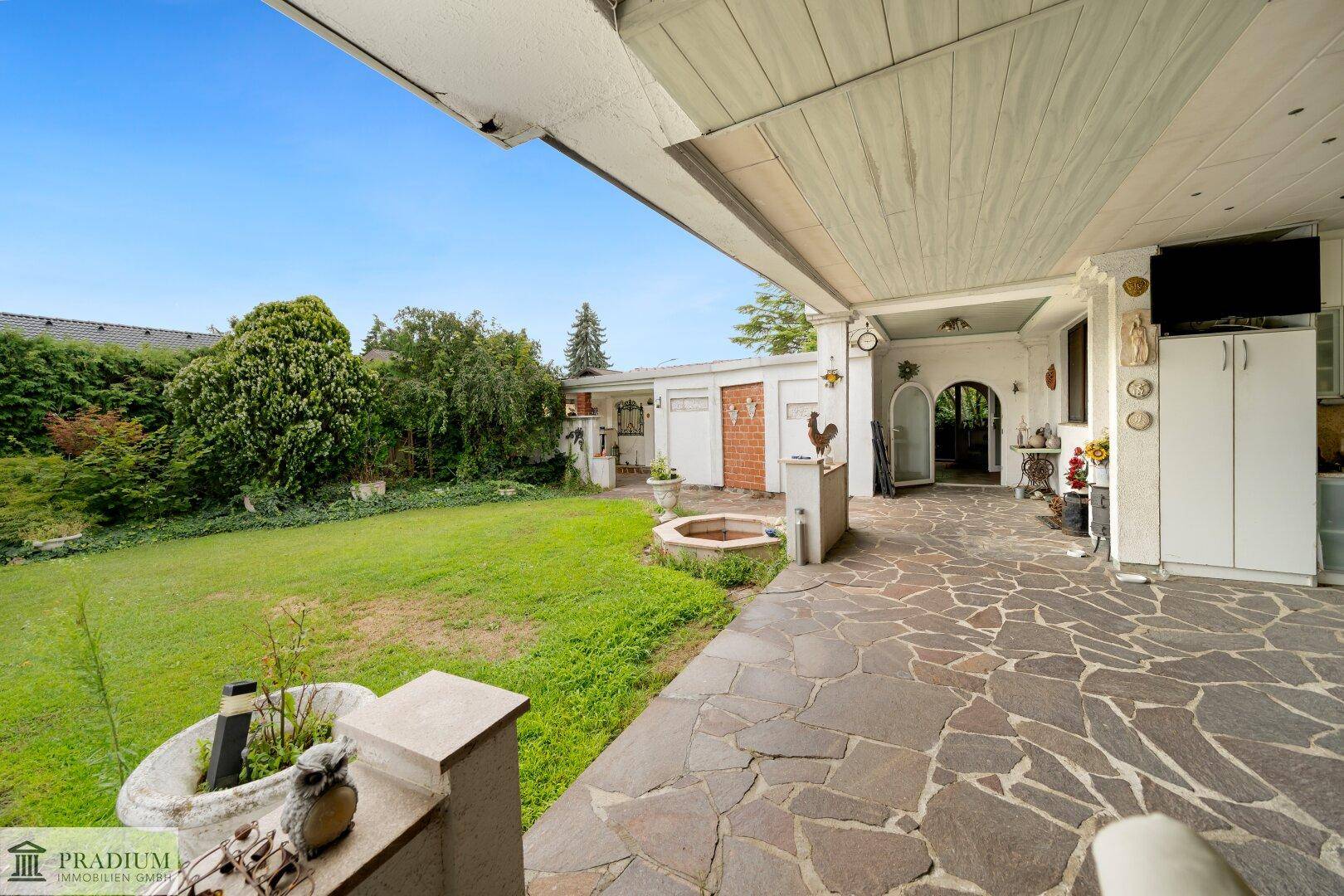 Geräumige überdachte Terrasse mit rustikalem Steinfliesenboden und Blick auf den grünen Garten.