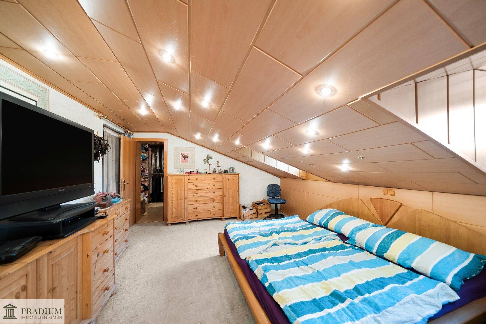 Helles Schlafzimmer im Dachgeschoss mit schräger Decke, Holztäfelung und Einbauschränken.
