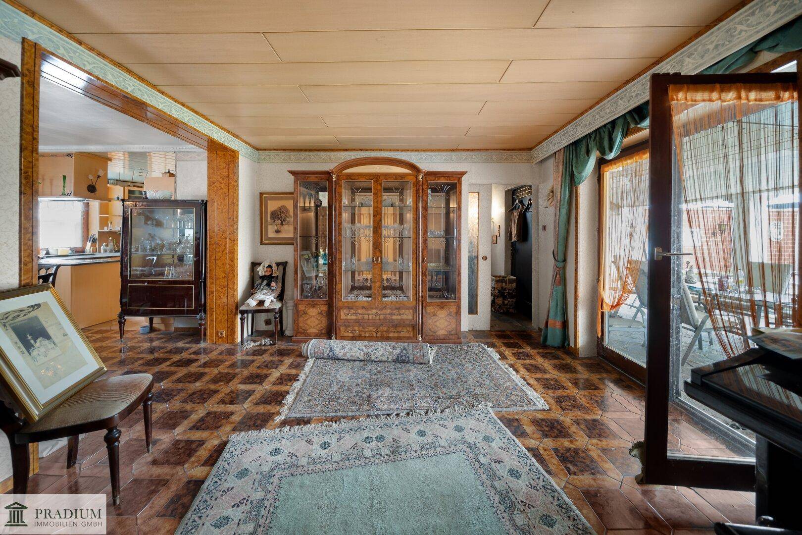 Traditionell eingerichtetes Wohnzimmer mit gemusterten Teppichen, Holzmöbeln und Zugang zur Terrasse.