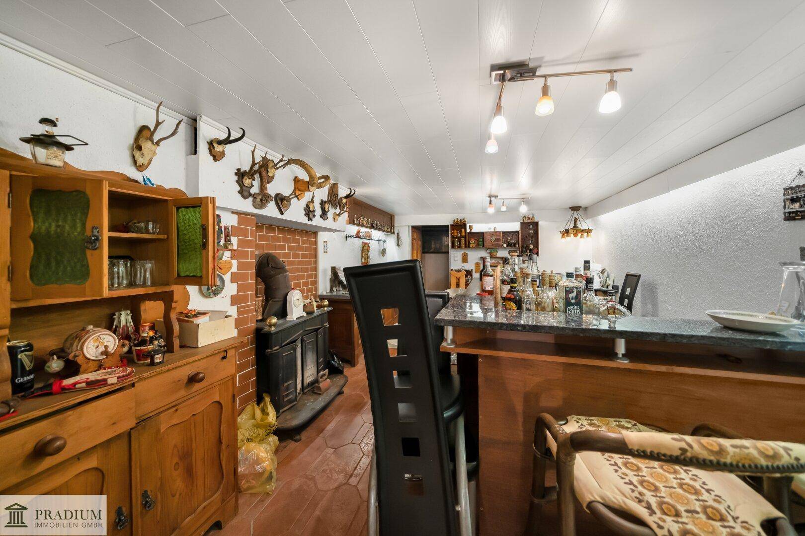 Rustikaler Partyraum im Keller mit Bar, Holzofen und Jagdtrophäen an den Wänden.
