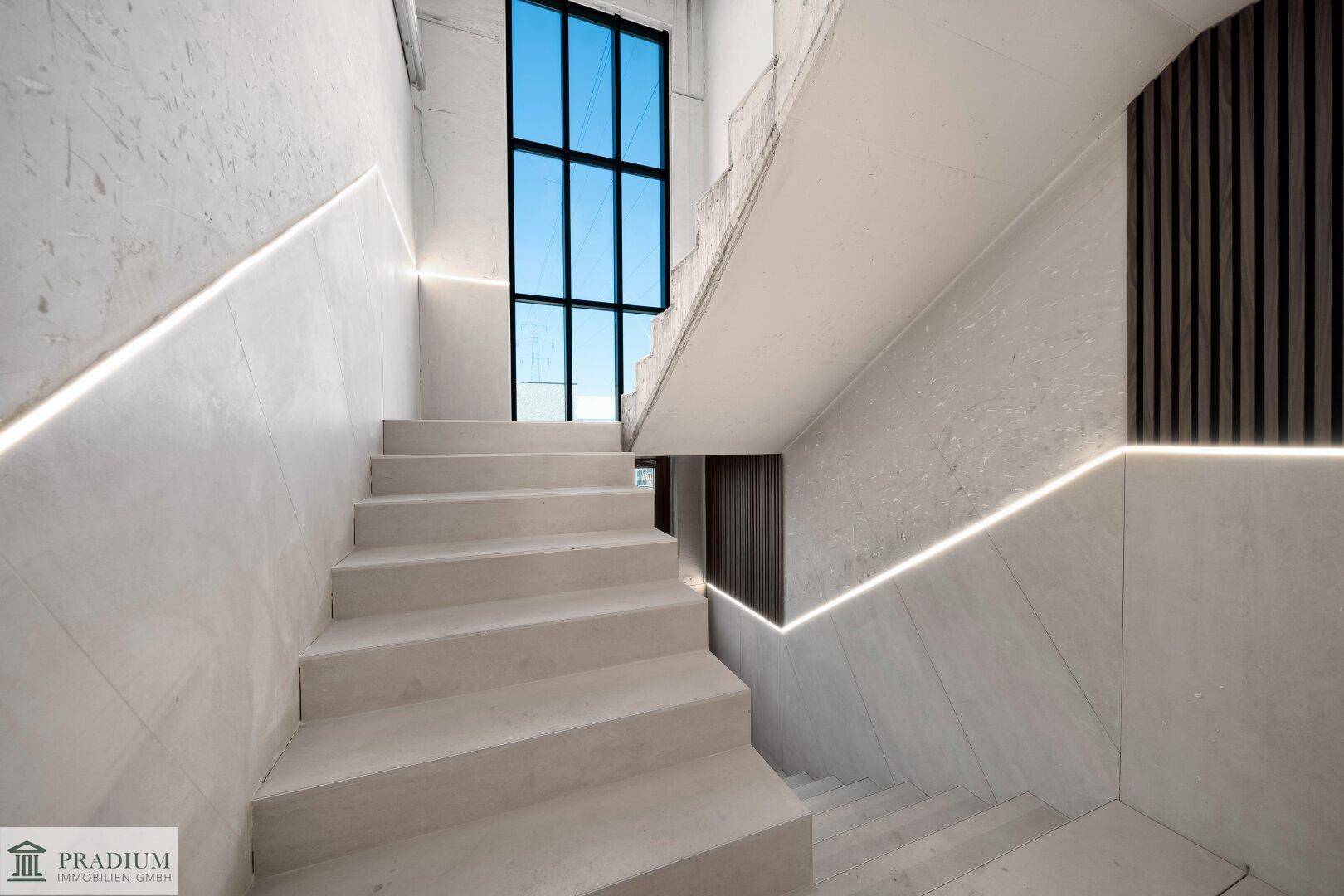 Modernes Treppenhaus mit indirekter Beleuchtung, großen Fenstern und eleganten Fliesen.