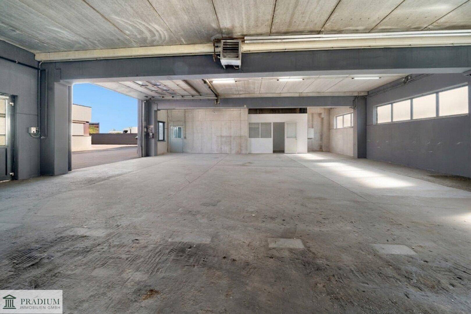 Geräumige Lagerhalle mit Betonboden, hohen Decken und Zugang zu einem Außenbereich.