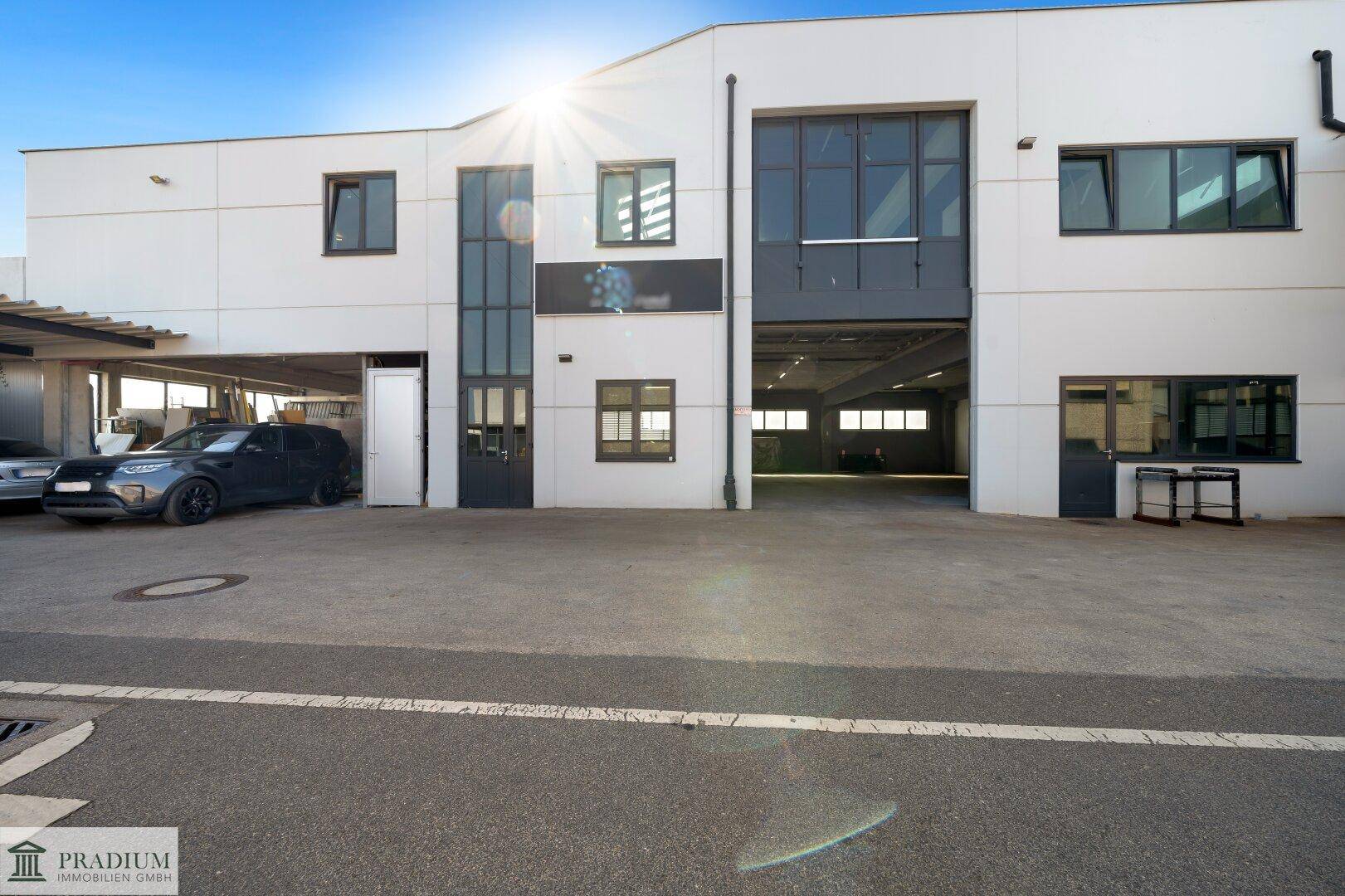 Moderne Gewerbeimmobilie mit großen Fenstern, Parkplätzen und Zufahrt für Fahrzeuge.