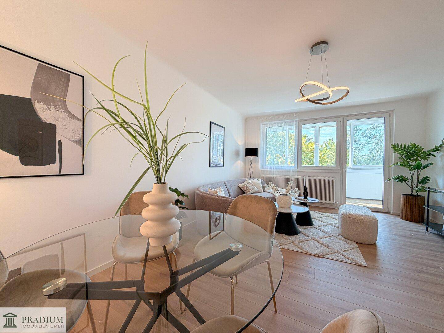 Offener Wohn-Essbereich mit modernem Glastisch, beigem Sofa und Zugang zu einem Balkon.