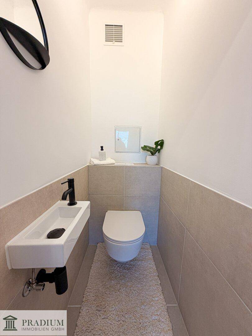 Separates Gäste-WC mit wandhängender Toilette, kleinem Waschbecken und Fliesenboden.